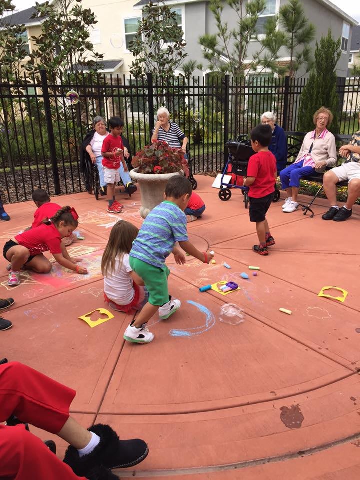 Children and seniors engage in chalk drawing during a community gathering outdoors.