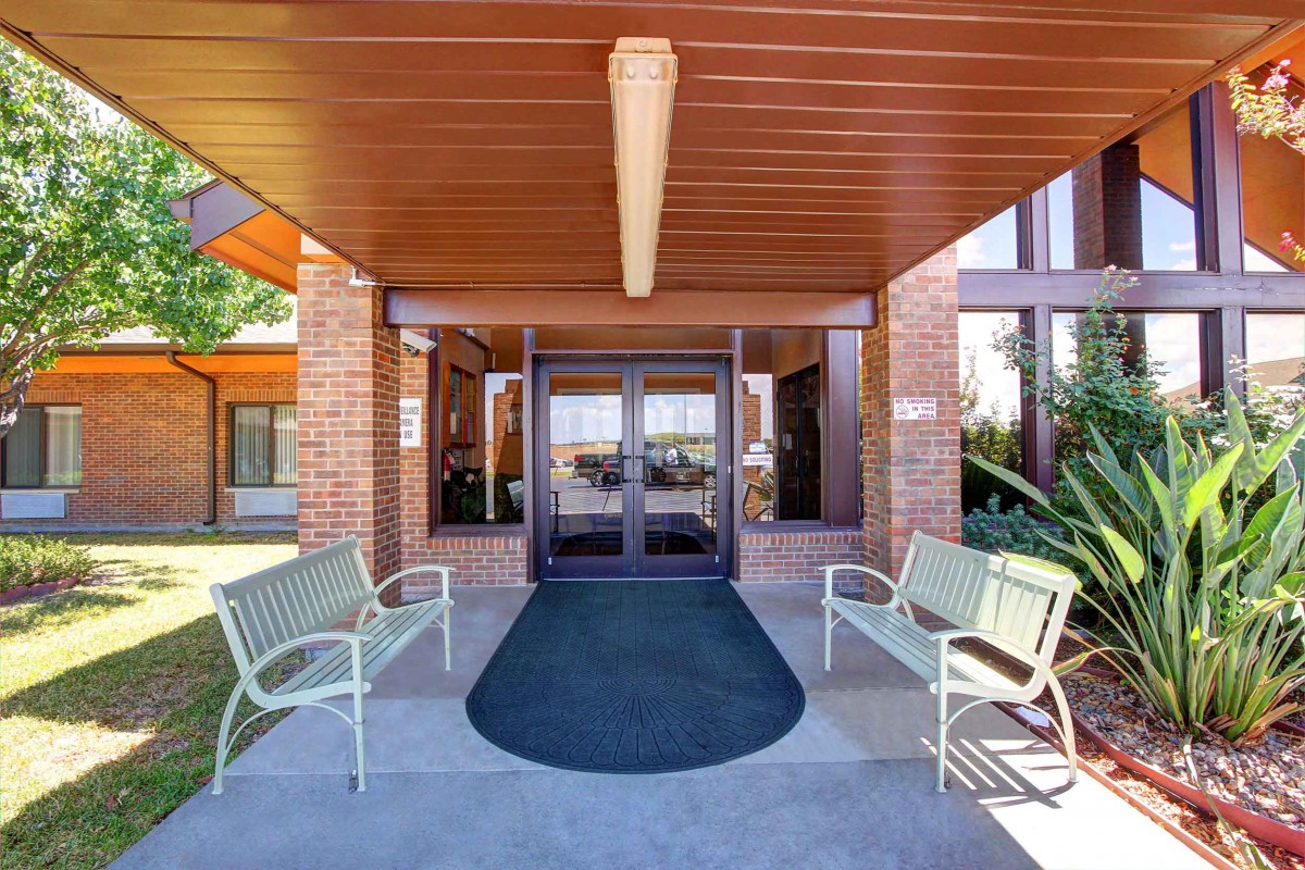The entrance of a brick building with benches and a wooden ceiling.