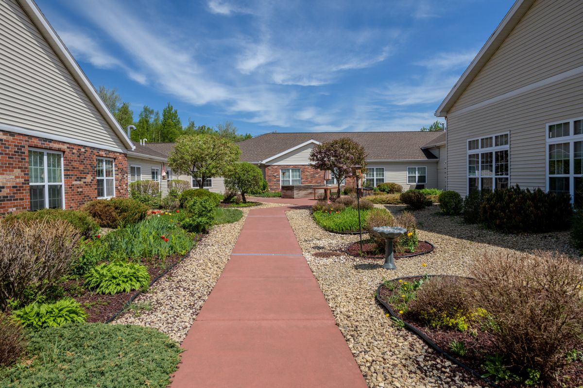 A serene residential pathway surrounded by well-maintained gardens and landscaping under a blue sky.