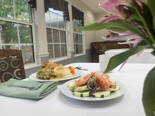 A beautifully arranged lunch featuring a fresh salad with cucumber and garnishes, complemented by a side dish, set in a well-lit dining area.