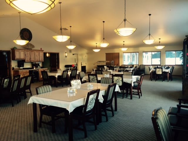 Spacious dining room with neatly arranged tables and chairs under elegant chandeliers.
