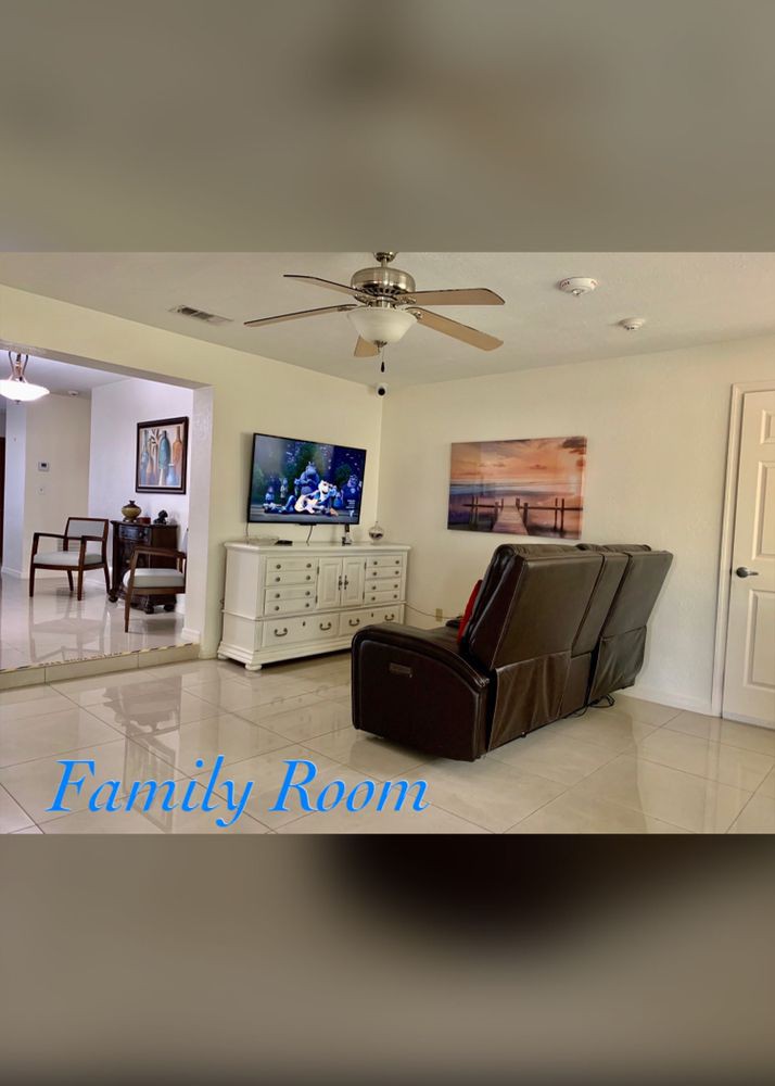 A cozy family room featuring a reclining sofa, ceiling fan, and a television set on a white cabinet.