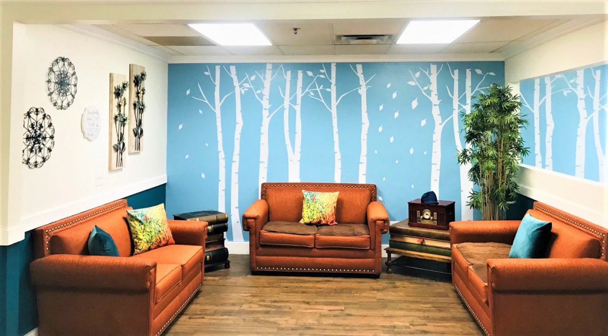 A cozy living room with orange sofas, a blue wall featuring a tree mural, and decorative pillows.