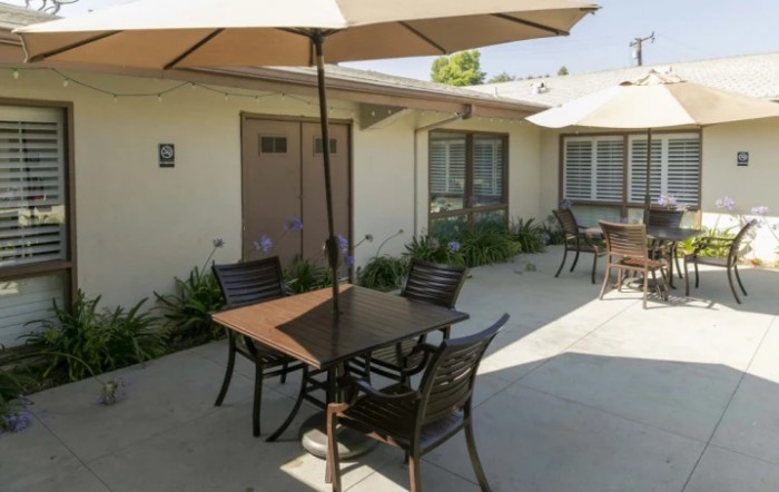 A sunny patio area with tables, chairs, and umbrellas outside a building.