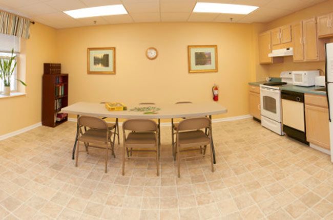 A simple kitchen setup with a table, chairs, and appliances.