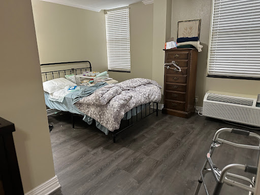 A cozy, unmade bedroom featuring a metal bed frame, a wooden dresser, and natural light from the window.
