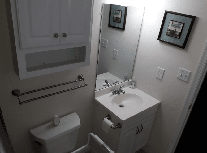A compact bathroom featuring a sink with a mirror above it, a toilet, a wall cabinet, and framed artwork on the walls.