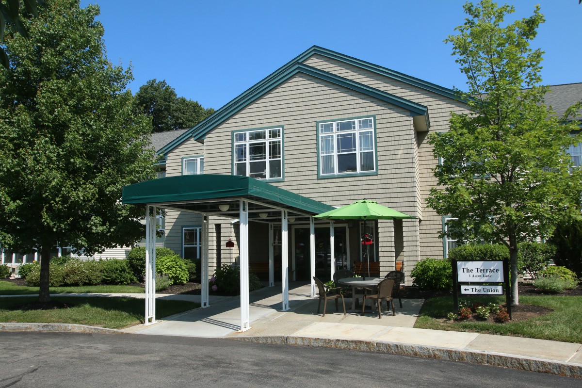 A residential building with a green awning and outdoor seating area surrounded by trees.