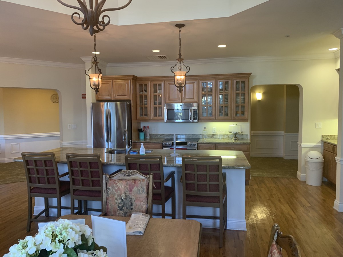 A modern kitchen with a large island counter and dining area, featuring stainless steel appliances and elegant pendant lighting.