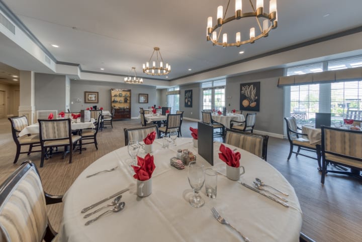 An elegantly set dining room with round tables, decorated with red flowers and sophisticated table settings.
