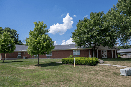 A residential building with a well-maintained lawn and trees under a bright blue sky.