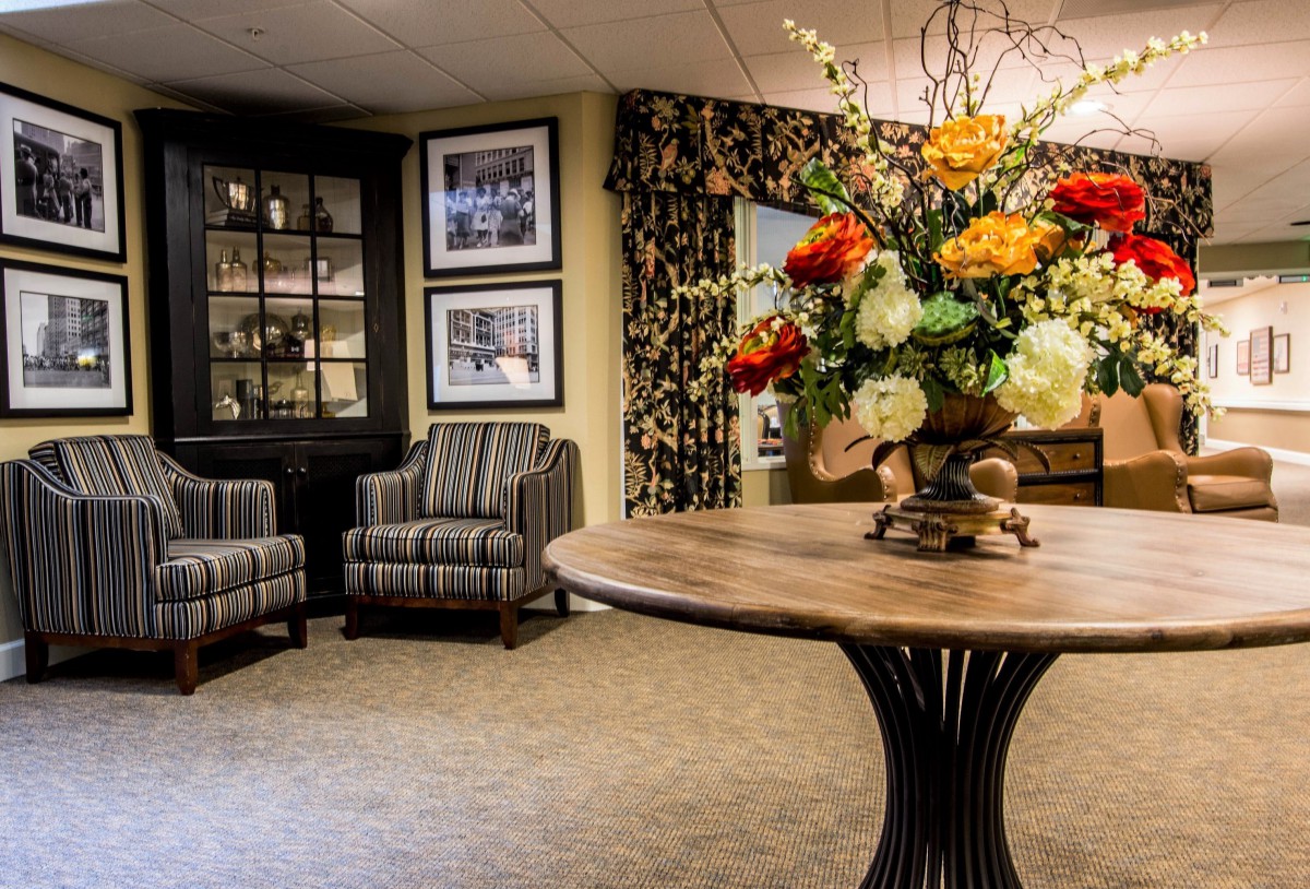 A cozy lounge area with elegant decor, featuring armchairs, a floral arrangement on a table, and framed pictures on the wall.