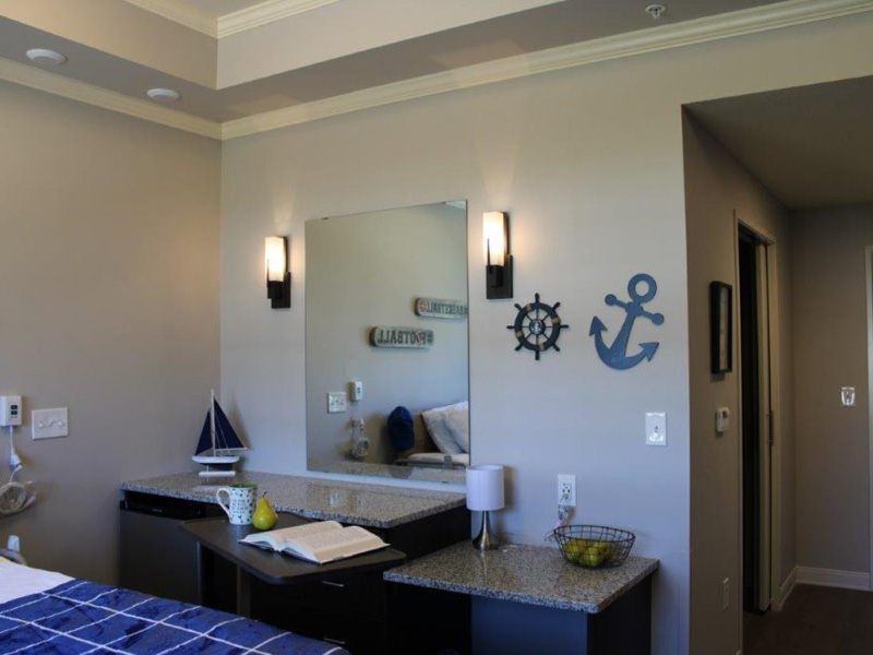 A bedroom with nautical-themed decor, featuring an anchor and ship wheel wall art, a mirror, and a sailboat model.
