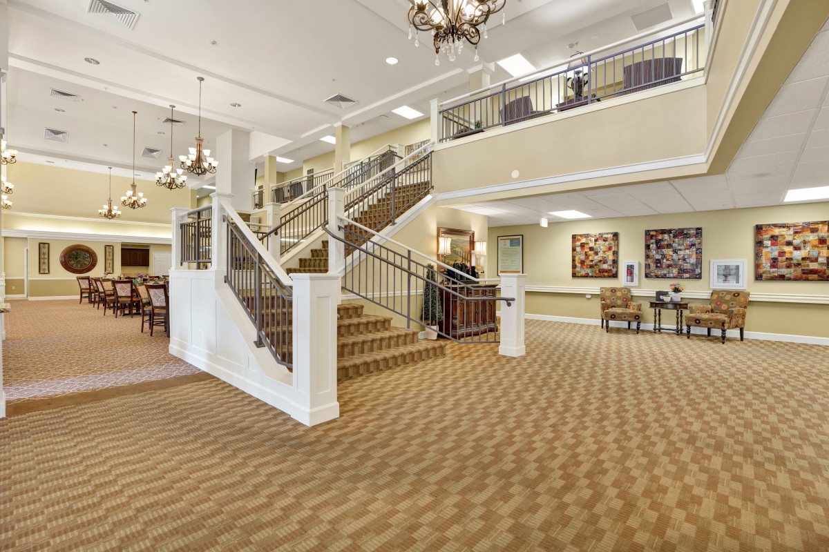 A spacious lobby with a central staircase, chandeliers, and a carpeted floor.
