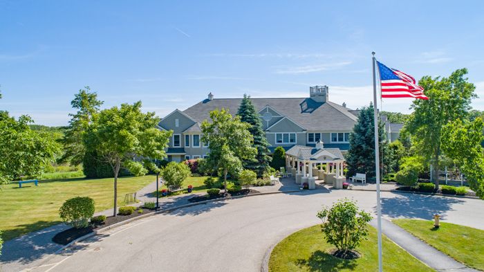 A large mansion surrounded by lush greenery and a circular driveway under a clear blue sky.