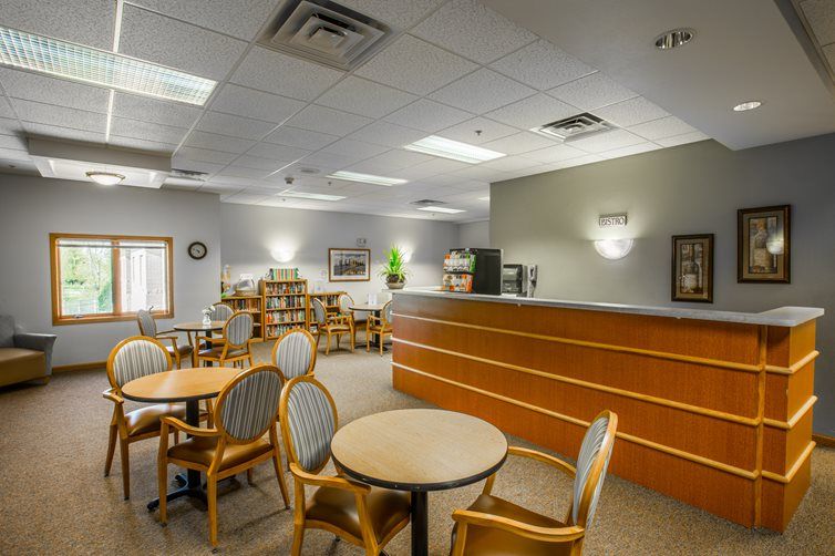 A spacious waiting area with tables and chairs, featuring a reception desk and decorative artwork on the walls.
