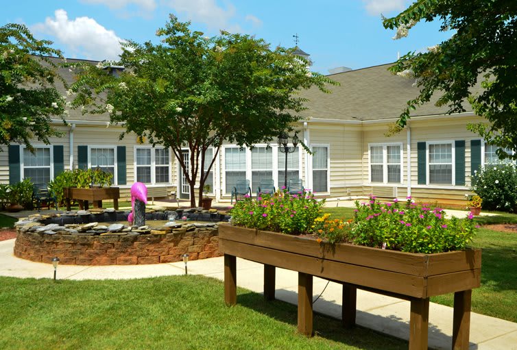 A sunny outdoor area featuring raised garden beds in front of a single-story building.