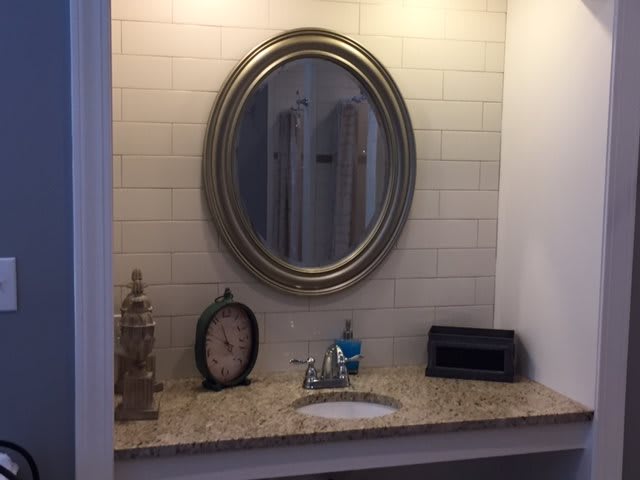 A well-lit bathroom countertop with an oval mirror, sink, and decorative items.