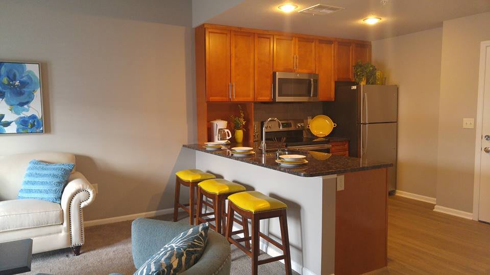 A modern kitchen with wooden cabinets, a sleek countertop, and vibrant yellow bar stools.