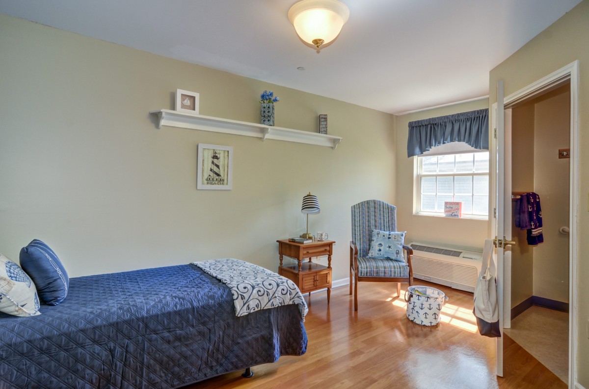 A cozy bedroom with a single bed, wooden floor, and a chair by the window.