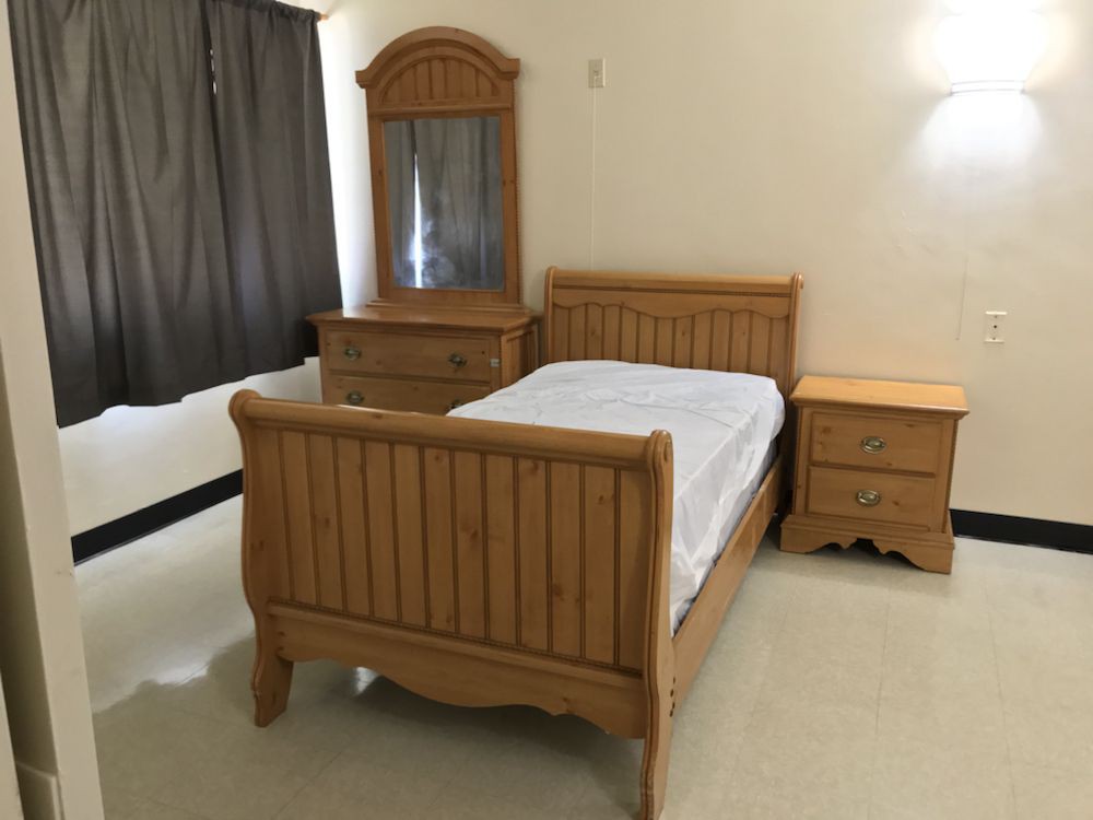 A simple bedroom with wooden furniture, including a bed, dresser with mirror, and nightstand.