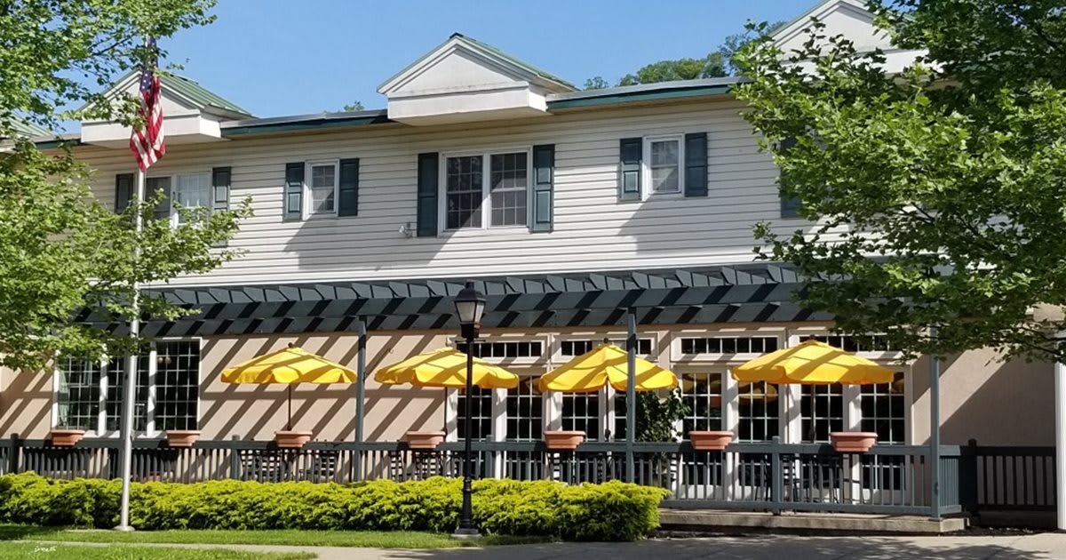 A restaurant with outdoor seating featuring yellow umbrellas and a white building facade on a sunny day.
