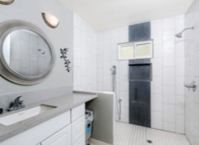 A modern bathroom featuring a round mirror, sink, and shower area with tiled walls.