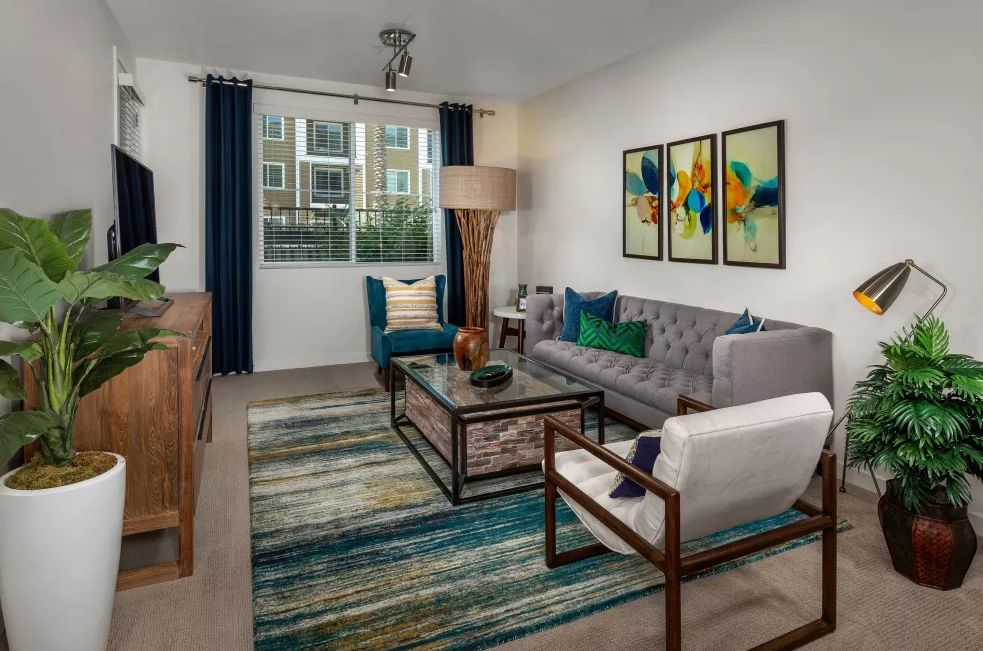 A contemporary living room featuring colorful artwork, a plush sofa, cozy armchair, and a stylish coffee table over a patterned rug.