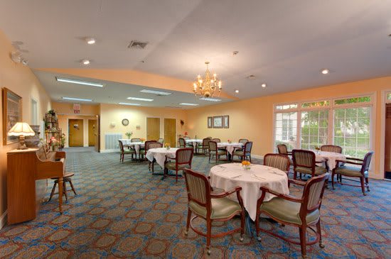 A well-lit dining room featuring tables with white cloths and elegant chairs, illuminated by a chandelier.