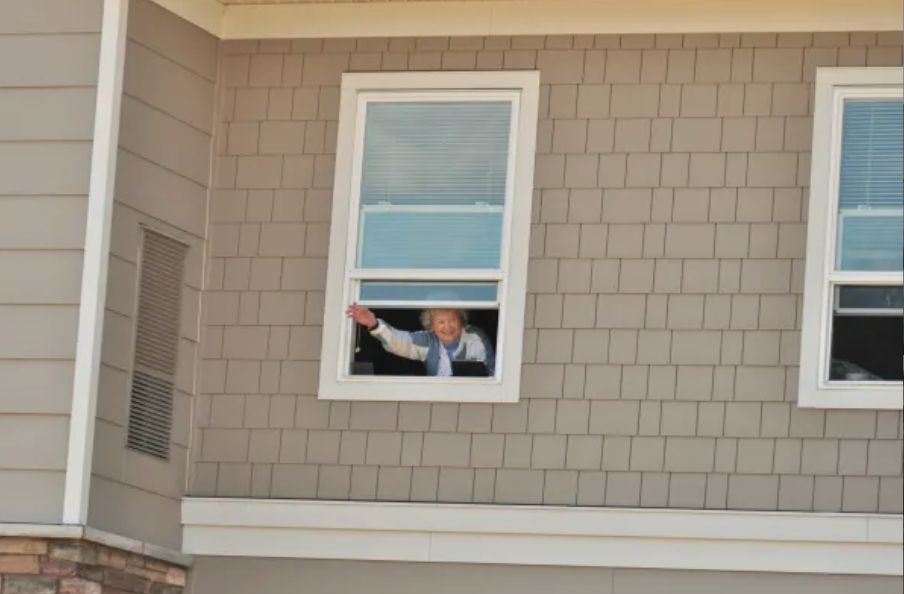 A person waving from inside a house through an open window.