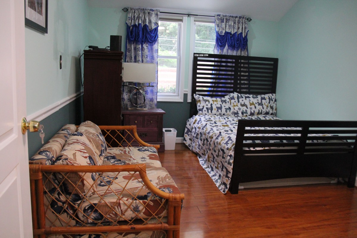 A cozy bedroom with a bed, sofa, and wooden flooring.