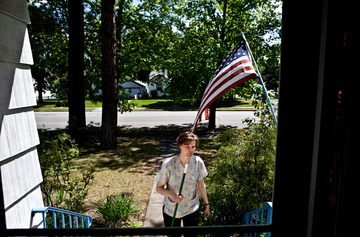 A woman walks towards her house with an American flag gently waving in the background.