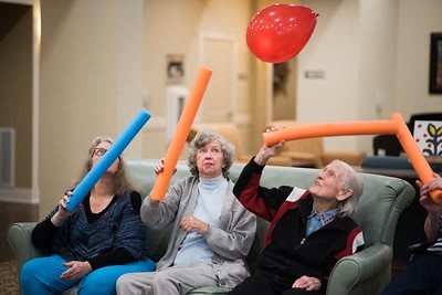 A group of seniors enjoying a playful indoor activity with balloons and noodle toys.