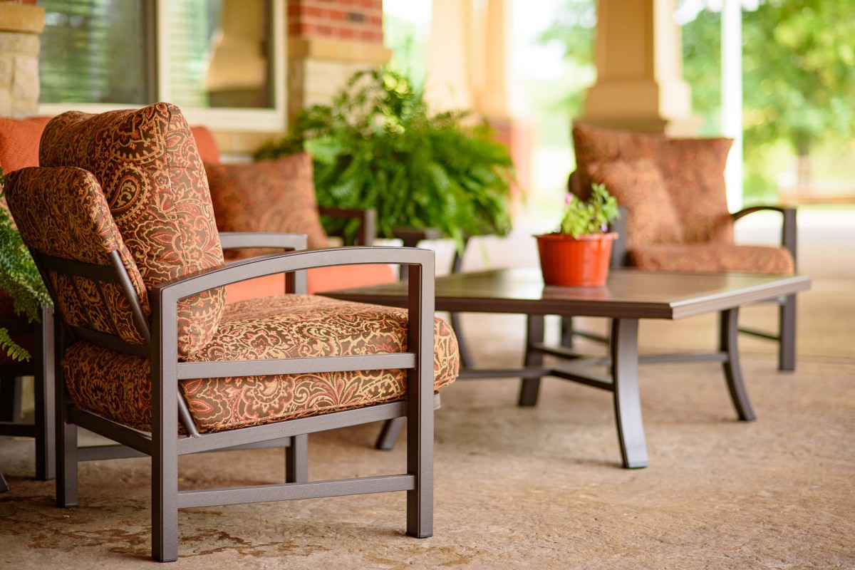 A cozy outdoor patio setup with cushioned chairs, a table, and potted plants.