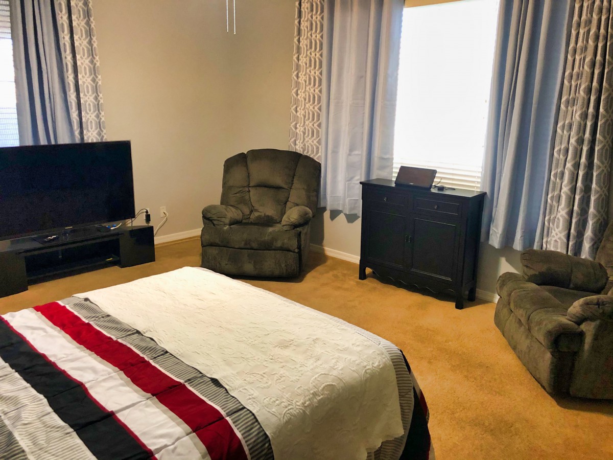 A cozy bedroom with a bed, armchair, and TV set near a window with curtains.