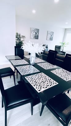 A modern dining room with a stylish table set featuring intricate placemats and a centerpiece vase filled with white flowers.