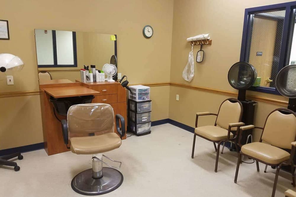 An empty hair salon with a styling chair, mirror, and various salon equipment.