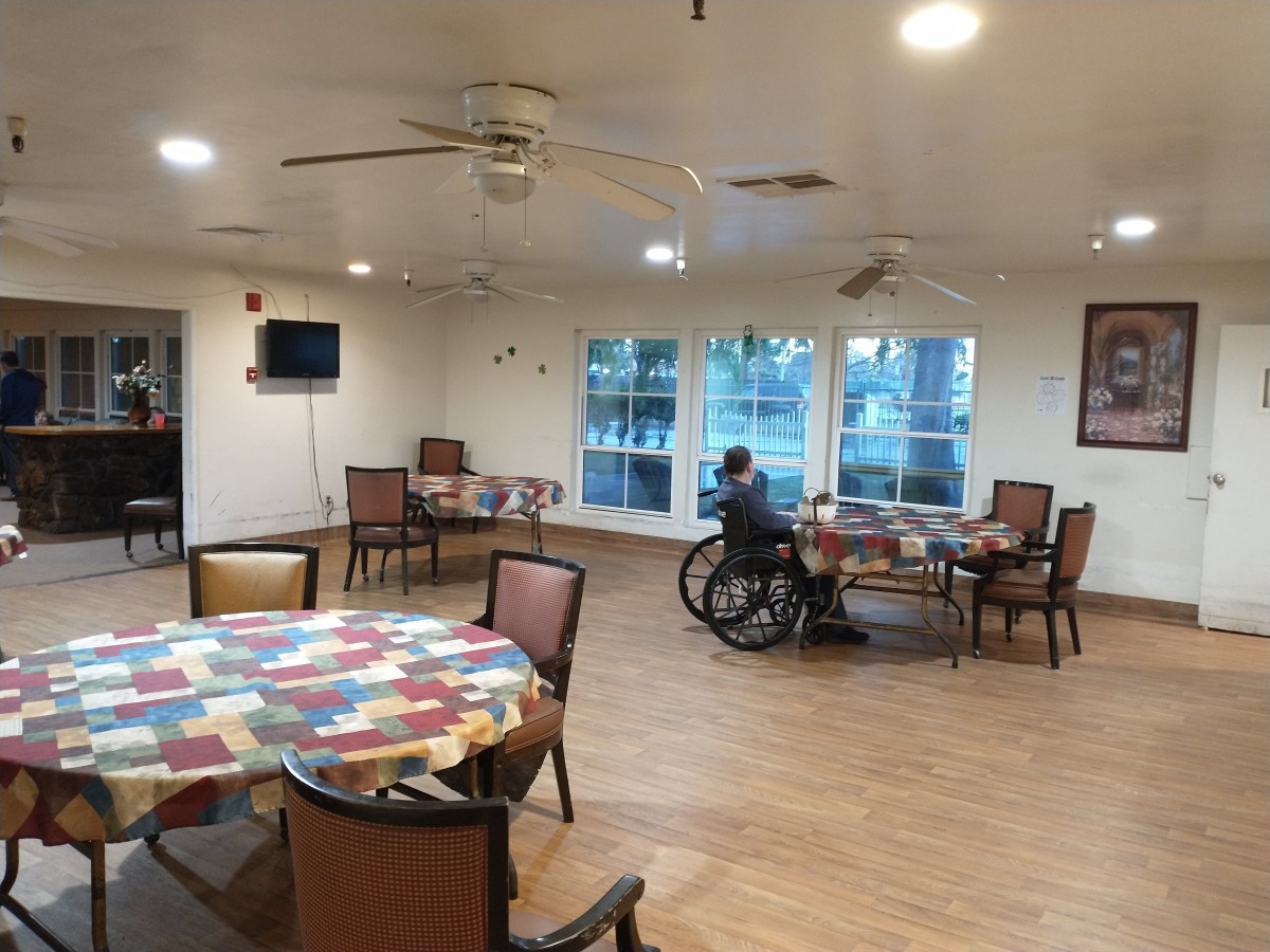 A quiet dining area in a nursing home with tables, chairs, and a resident in a wheelchair.