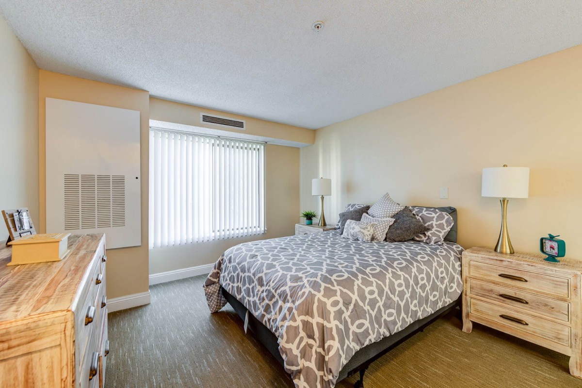 A cozy bedroom with a neatly made bed, decorative pillows, a lamp on the bedside table, and natural light coming through the window.