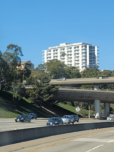 A view of a modern building situated above a busy highway, surrounded by greenery.