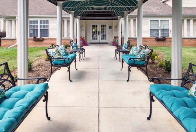 A covered walkway leading to a building entrance, lined with benches adorned with teal cushions.