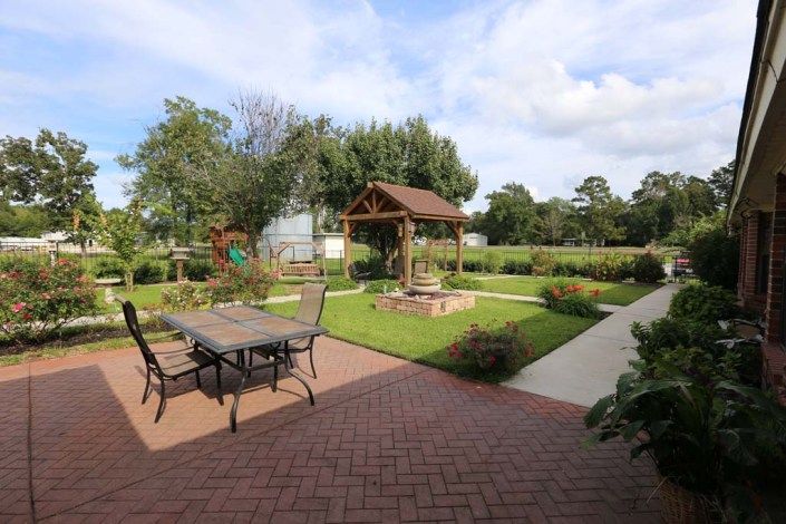 A tranquil garden scene featuring a patio with outdoor furniture, a decorative well, and lush landscaping.