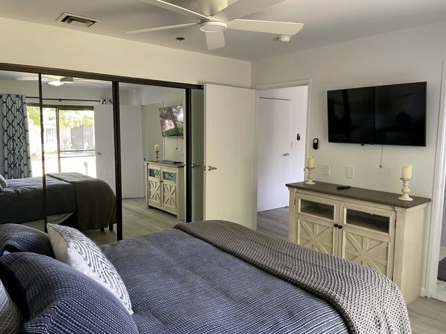 Modern bedroom interior with a wall-mounted TV and mirrored closet doors.