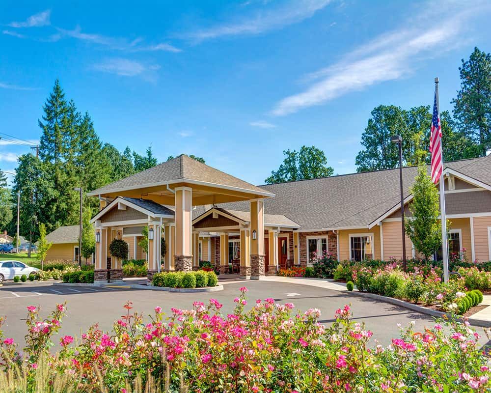 A beautiful building entrance surrounded by colorful flowers and greenery, with a clear blue sky in the background.