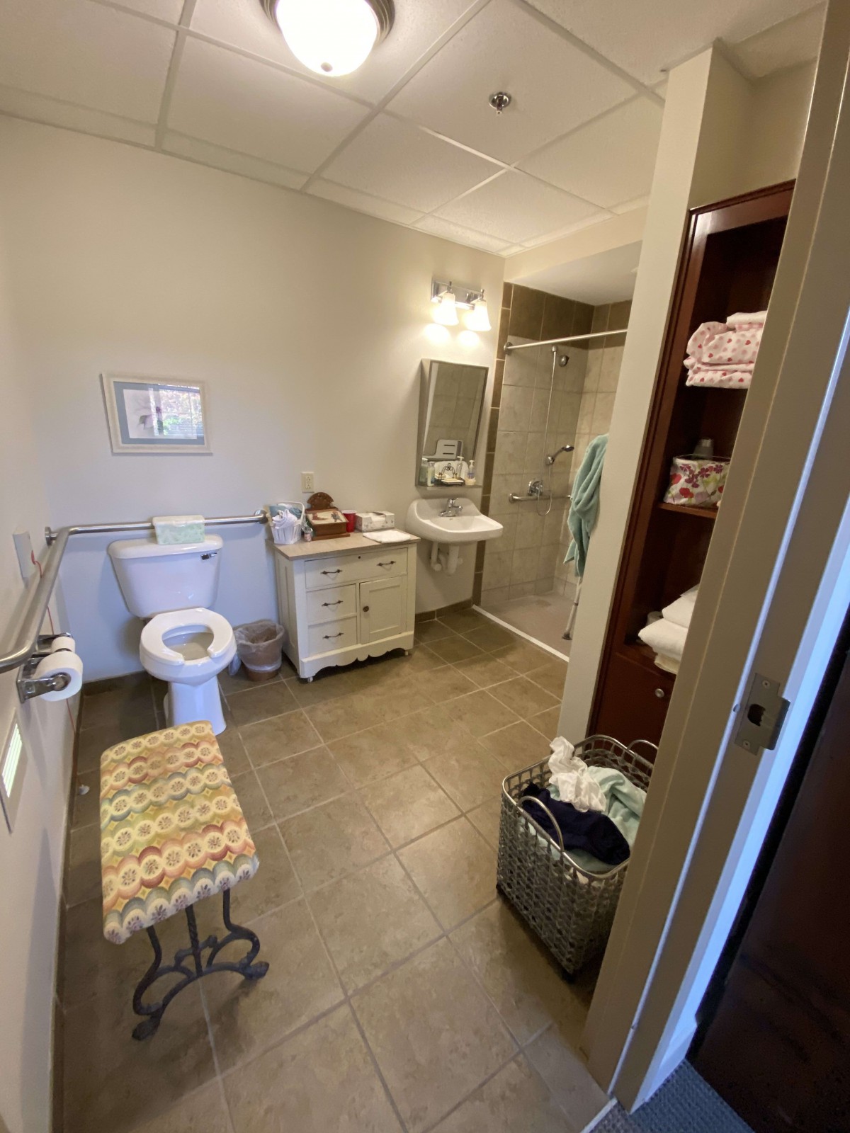 A spacious bathroom with a toilet, sink, and shower, featuring ample storage and a laundry basket.