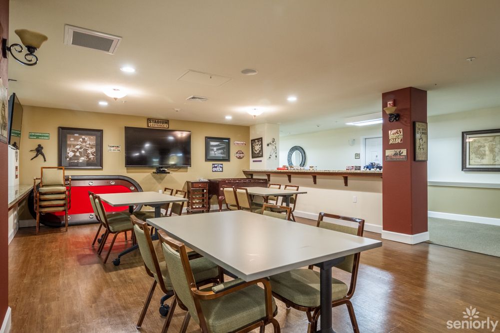 Cozy dining area with tables, chairs, and a television, complemented by a bar counter and framed pictures on the walls.