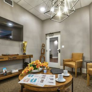 A modern waiting room featuring comfortable seating, a television, and a stylish chandelier.