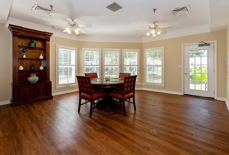 A spacious dining room with wood flooring, featuring a round table and chairs surrounded by large windows.