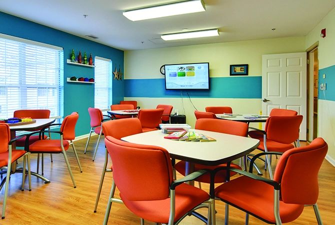 A brightly colored classroom with red chairs, tables, and a television on the wall.