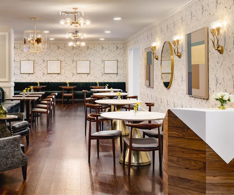 A modern restaurant interior featuring elegant chandeliers, wooden flooring, and neatly arranged tables and chairs.
